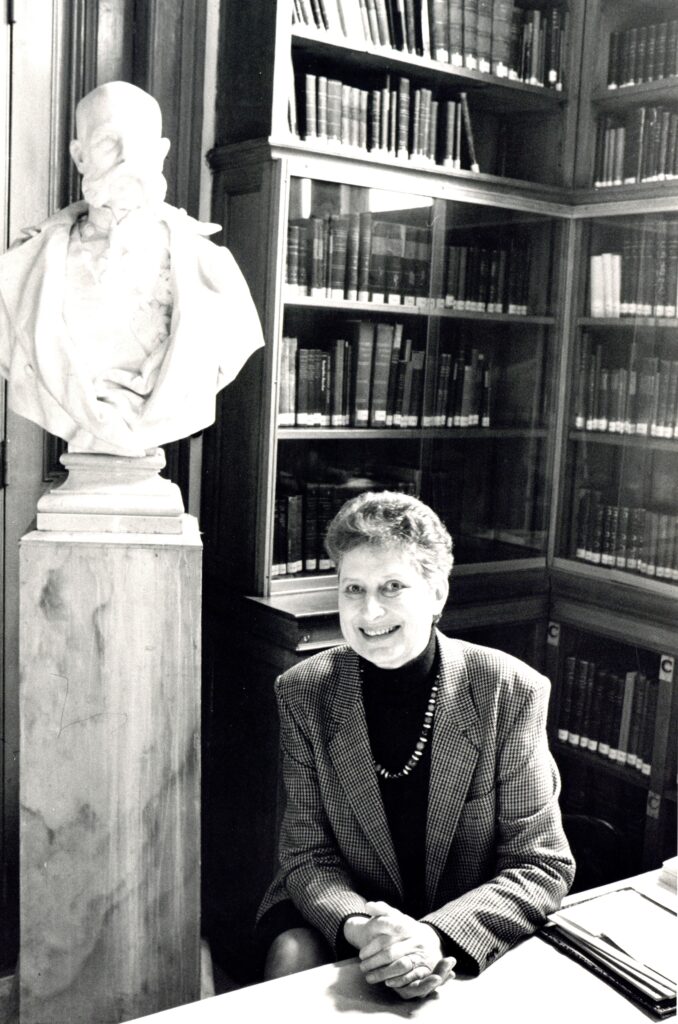 Veronika Mitsopoulos-Leon dans la bibliothèque de l’Institut autrichien d’archéologie à Athènes, près d’un portrait de l’empereur François Joseph Ier, qui a financé la construction du bâtiment de l’institut (années 1990, archives privées Mitsopoulos).